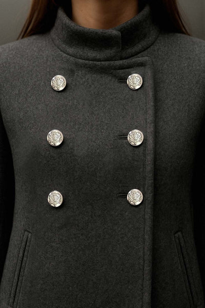 Abrigo cruzado de cuello alto, bolsillos delanteros y manga larga. Cierre frontal con doble cruce de botones en contraste.