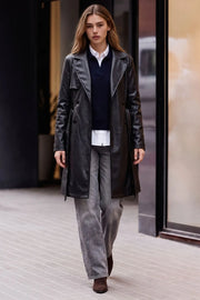 Abrigo trench de efecto piel, fit recto, con solapa, bolsillos delanteros con vivos, detalle de bata delantera y manga larga. Trabillas, cinturón amarrable del mismo tejido y cierre frontal con doble cruce de botón.
