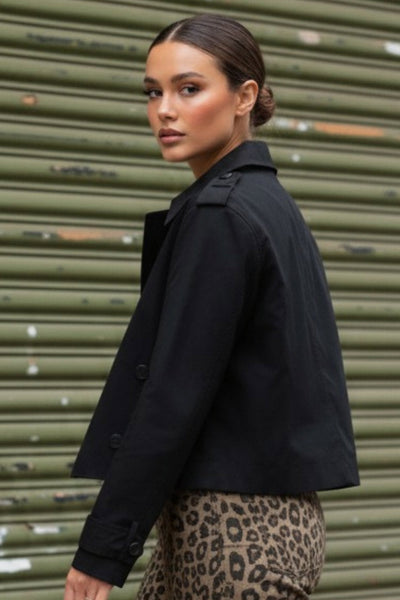 Abrigo trench corto de fit recto, cuello solapa, manga larga, trabillas con botón en puños y hombros. Bolsillos delanteros con vivos y cierre frontal con doble cruce de botones.