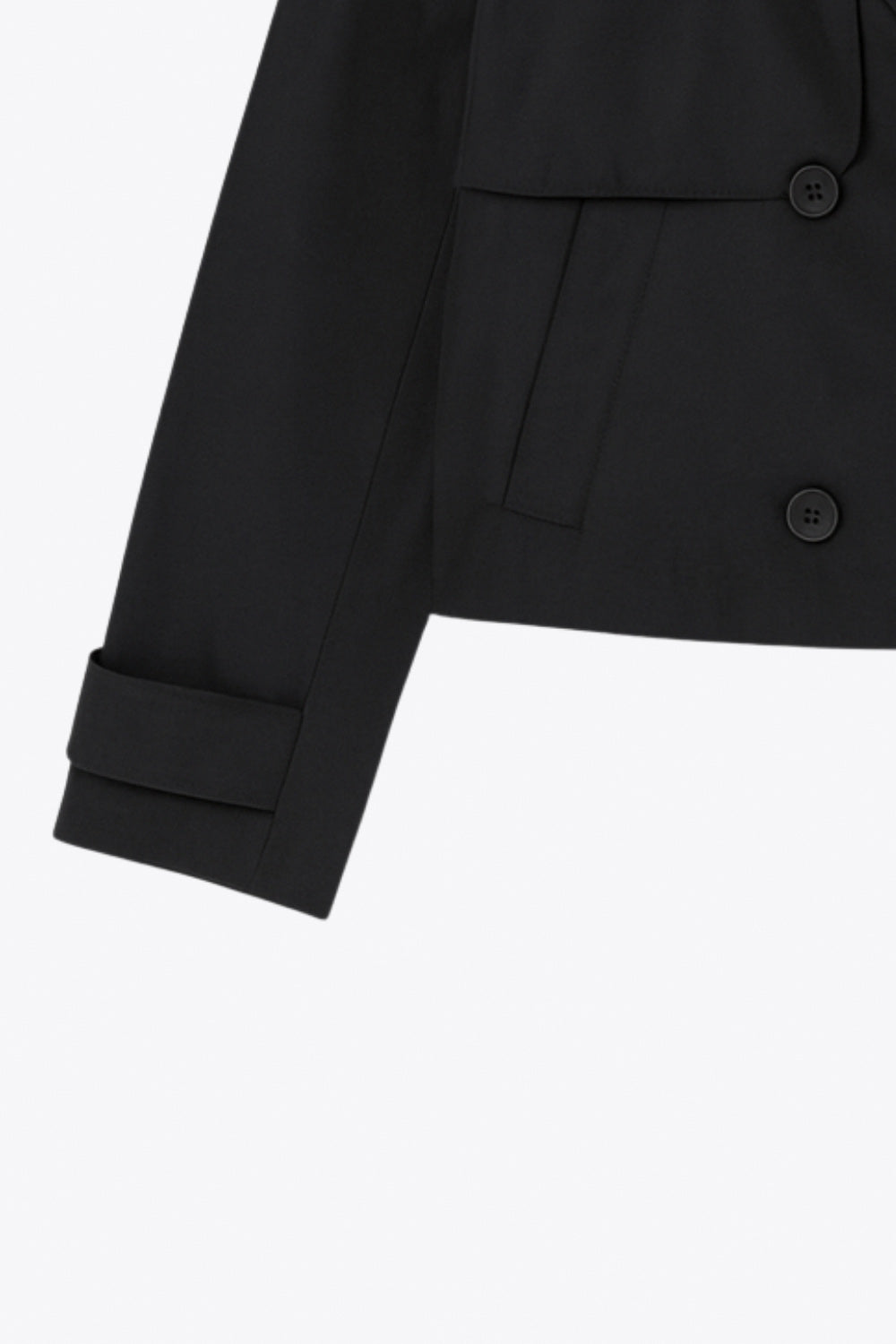 Abrigo trench corto de fit recto, cuello solapa, manga larga, trabillas con botón en puños y hombros. Bolsillos delanteros con vivos y cierre frontal con doble cruce de botones.