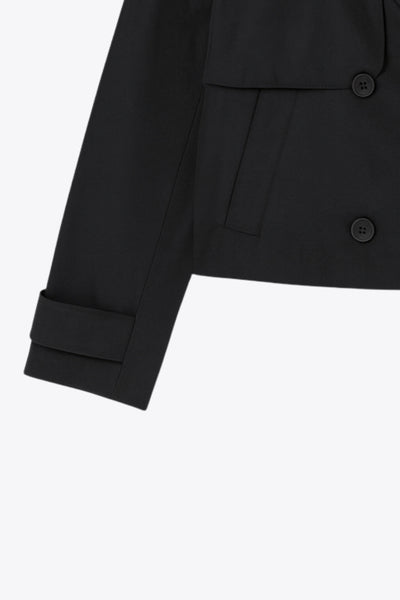 Abrigo trench corto de fit recto, cuello solapa, manga larga, trabillas con botón en puños y hombros. Bolsillos delanteros con vivos y cierre frontal con doble cruce de botones.