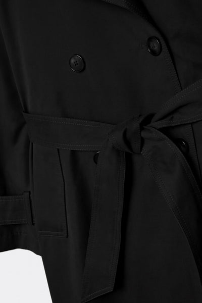 Abrigo trench corto de fit recto, con solapa, bolsillos delanteros con vivos, detalle de bata trasera y manga larga. Trabillas, cinturón amarrable del mismo tejido y cierre frontal con doble cruce de botones en contraste. Detalle de trabilla y botón en hombros, bata trasera y puños.