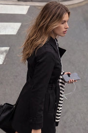 Abrigo trench corto de fit recto, con cuello solapa, bolsillos delanteros con vivos, detalle de bata trasera y manga larga. Trabillas, cinturón amarrable del mismo tejido y cierre frontal con doble cruce de botones en contraste. Detalle de trabilla y botón en hombros, bata trasera, cuello y puños.
