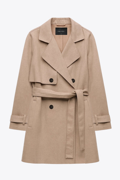 Abrigo trench corto de fit recto, con solapa, bolsillos delanteros con vivos, detalle de bata frontal con botón decorativo y trasera. Manga larga con trabilla en puños, cinturón amarrable del mismo tejido y cierre frontal con doble cruce de botones en contraste.