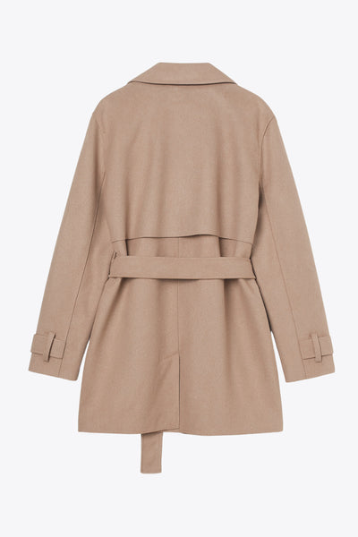 Abrigo trench corto de fit recto, con solapa, bolsillos delanteros con vivos, detalle de bata frontal con botón decorativo y trasera. Manga larga con trabilla en puños, cinturón amarrable del mismo tejido y cierre frontal con doble cruce de botones en contraste.