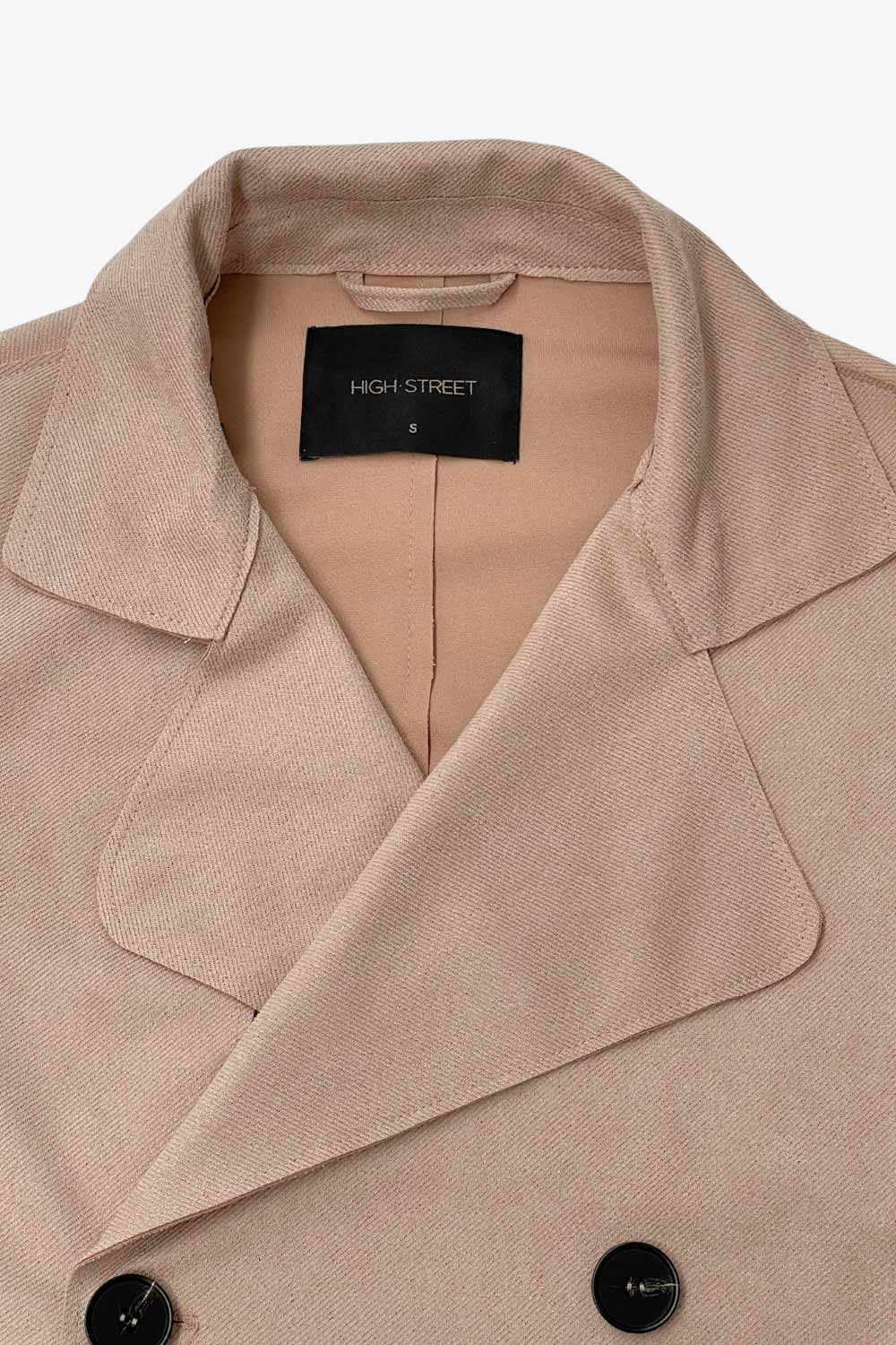 Abrigo trench corto de fit recto, con solapa, bolsillos delanteros con vivos, detalle de bata frontal con botón decorativo y trasera. Manga larga con trabilla en puños, cinturón amarrable del mismo tejido y cierre frontal con doble cruce de botones en contraste.