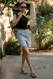 Bermuda corta de denim, fit recto, cintura media con pretina y trabillas, bolsillos delanteros y traseros de parche. Cierre frontal con botón y cremallera oculta. Detalle de rotos en bajo.