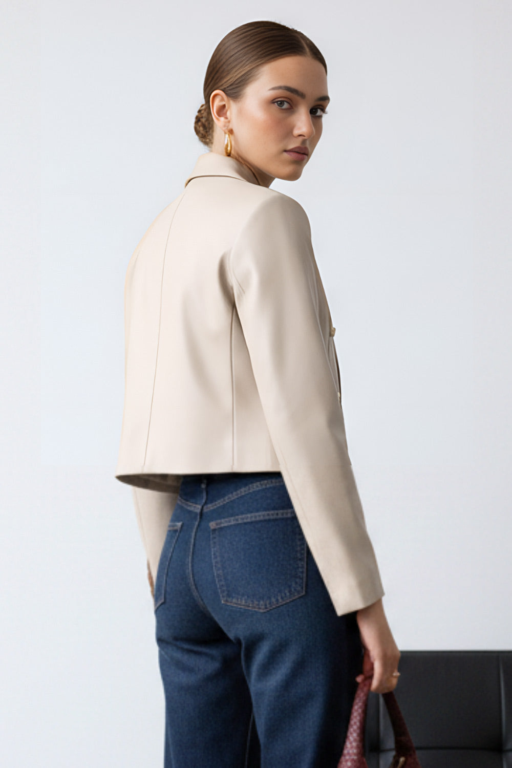 Blazer corto abierto de efecto piel, fit recto, con hombreras y solapa, manga larga y botones decorativos frontales en contraste.