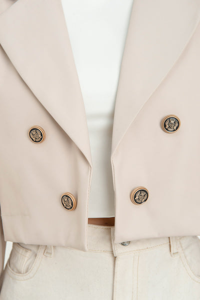 Blazer corto abierto de efecto piel, fit recto, con hombreras y solapa, manga larga y botones decorativos frontales en contraste.