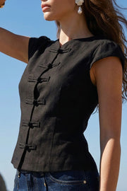 Blusa corta de fit ajustado, cuello mao, manga corta con plisados en hombros, cierre frontal con botones y detalle de lazo amarrable posterior.