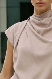 Blusa fluida de manga corta seguida, cuello mock seguido con plisados decorativos en hombro y cuello. Cierre posterior con botones y ojales.