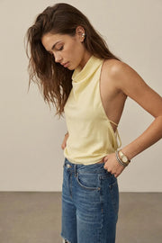 Blusa corta de lino, fit fluido, sin mangas, cuello halter fluido con plisados, escote en espalda y lazo amarrable posterior. Cierre posterior con botón y ojal.