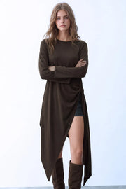 Blusa larga de fit fluido, cuello barco, manga larga amplia, bajo asimétrico, plisados en costado con abertura y nudo decorativo, cierre posterior con botón y ojal.