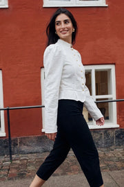 Blusa de fit ajustado, manga larga con hombros abullonados, cuello mao, pinzas frontales, peplum con olanes en bajo y cierre frontal con hilera de botones en contraste.