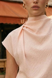 Blusa de cuello alto fluido, plisados en hombro, manga corta seguida y fit recto. Cierre posterior con botón y ojal.