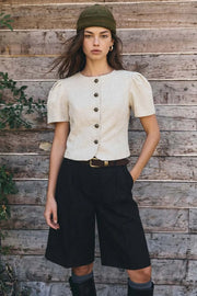 Blusa corta de fit ajustado, cuello redondo, manga corta con plisados en hombros, cortes frontales, bajo curveado frontal y cierre con hilera de botones en contraste.