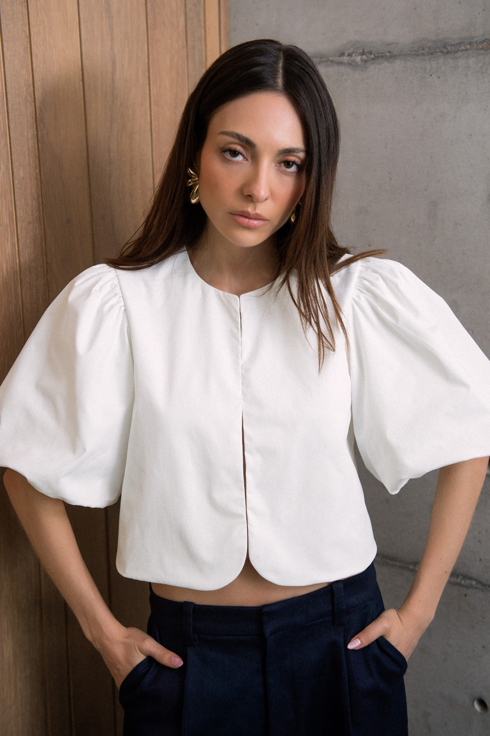 Blusa corta de fit recto, cuello redondo, manga corta amplia globo con volumen en borde, cierre frontal con broches ocultos y bajo curveado frontal.