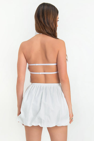 Blusa corta de cuello halter con escote fluido, sin mangas escote en espalda y cierre posterior con botón y ojal.