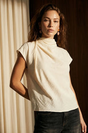Blusa fluida de manga corta seguida, cuello mock seguido con plisados decorativos en hombro y cuello. Cierre posterior con botones y ojales.