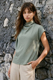 Blusa fluida de manga corta seguida, cuello mock seguido con plisados decorativos en hombro y cuello. Cierre posterior con botones y ojales.