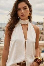 Blusa fluida de cuello alto halter, sin mangas, bajo asimétrico, escote frontal y en espalda.