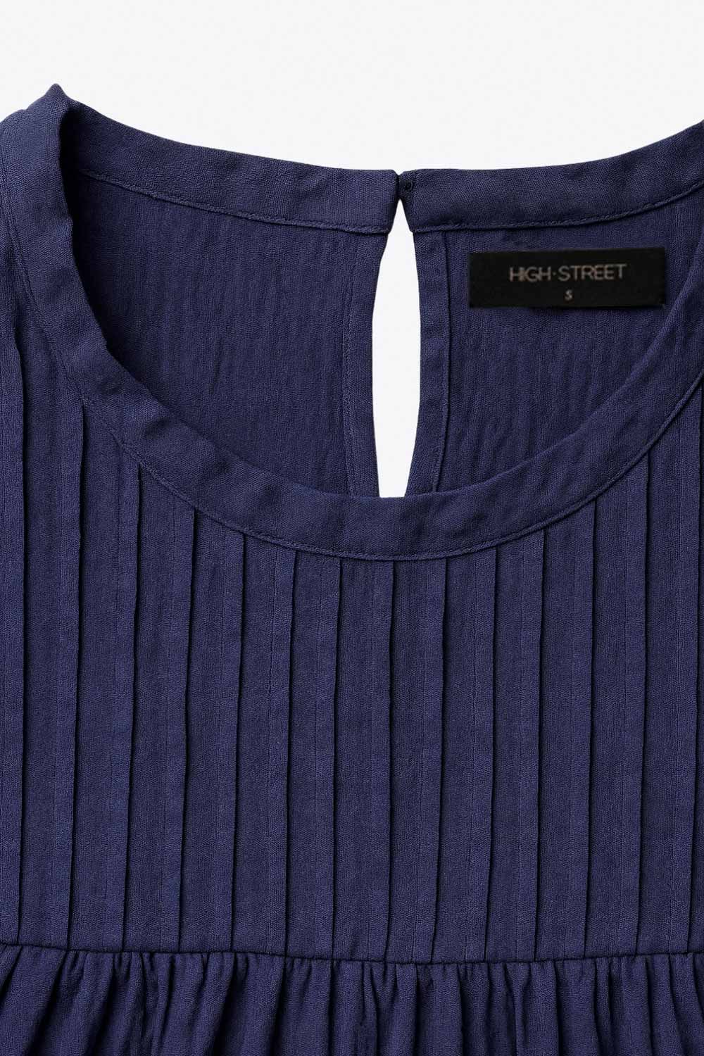 Blusa de fit recto, cuello redondo, sin mangas, olanes en sisa y costuras decorativas frontales con plisados. Cierre posterior con botón y ojal.