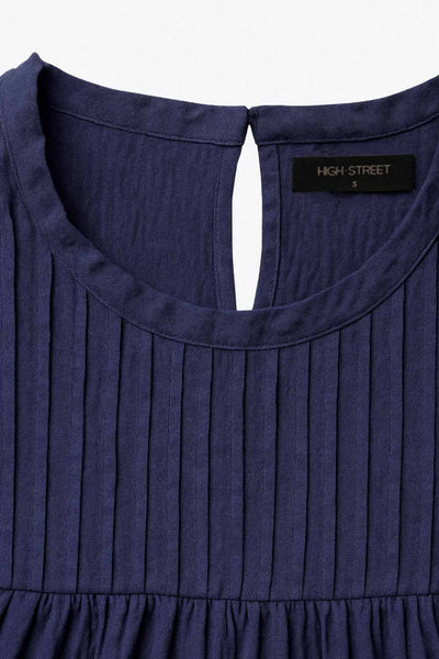 Blusa de fit recto, cuello redondo, sin mangas, olanes en sisa y costuras decorativas frontales con plisados. Cierre posterior con botón y ojal.