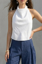 Blusa corta de fit fluido, sin mangas, cuello halter fluido con plisados, escote en espalda y lazo amarrable posterior. Cierre posterior con botón y ojal.