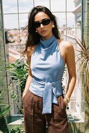 Blusa de fit recto, halter con cuello fluido, sin mangas, lazo amarrable en cintura, cierre posterior con botón y ojal.