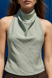 Blusa corta de fit fluido, sin mangas, cuello halter fluido con plisados, escote en espalda y lazo amarrable posterior. Cierre posterior con botón y ojal.
