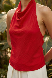 Blusa corta de fit fluido, sin mangas, cuello halter fluido con plisados, escote en espalda y lazo amarrable posterior. Cierre posterior con botón y ojal.