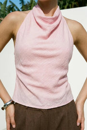 Blusa corta de fit fluido, sin mangas, cuello halter fluido con plisados, escote en espalda y lazo amarrable posterior. Cierre posterior con botón y ojal.