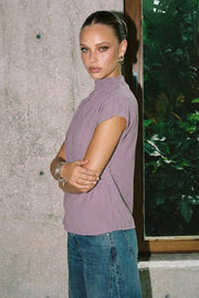 Blusa fluida de manga corta seguida, cuello mock seguido con plisados decorativos en hombro y cuello. Cierre posterior con botones y ojales.