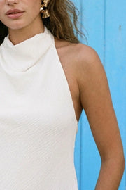 Blusa de cuello halter fluido, escote en espalda con lazo amarrable posterior, cierre con botón y ojal. Detalle de bajo frontal asimétrico.
