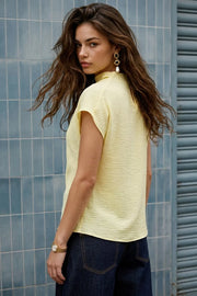Blusa de cuello alto fluido, plisados en hombros, manga corta seguida y fit recto. Cierre posterior con botón y ojal.