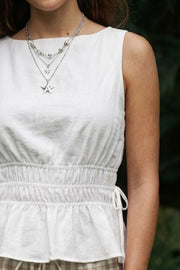 Blusa corta de cuello barco, sin mangas, rib con plisados en cintura, peplum con olanes en bajo y detalle de jaretas ajustables en costados. Cierre posterior con botón y ojal.