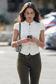Blusa corta de fit ajustado, pinzas frontales, manga corta abullonada con plisados en hombros, cuello mao y cierre frontal con botones en contraste. Detalle de peplum con olanes y bajo curveado frontal.
