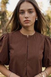 Blusa corta de fit recto, cuello redondo, manga corta amplia globo con volumen en borde, cierre frontal con broches ocultos y bajo curveado frontal.