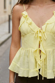 Blusa corta de tirantes delgados ajustables, escote v con olanes en borde, cortes frontales con plisados, peplum con olanes en bajo y cierre frontal con lazos amarrables.