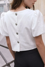Blusa corta de fit recto, cuello barco, manga corta abullonada y cierre posterior con hilera de botones en contraste.