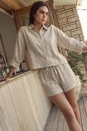Camisa corta de rayas, ligeramente oversized, cuello camisero, manga larga rolled up con trabilla ajustable y botón. Cierre frontal con hilera de botones y detalle de pinza de amplitud en espalda.