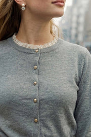 Cardigan de punto, fit recto, manga larga con rib en puños y cuello redondo. Cierre frontal con hilera de botones en contraste y detalle de encaje decorativo en cuello y puños.