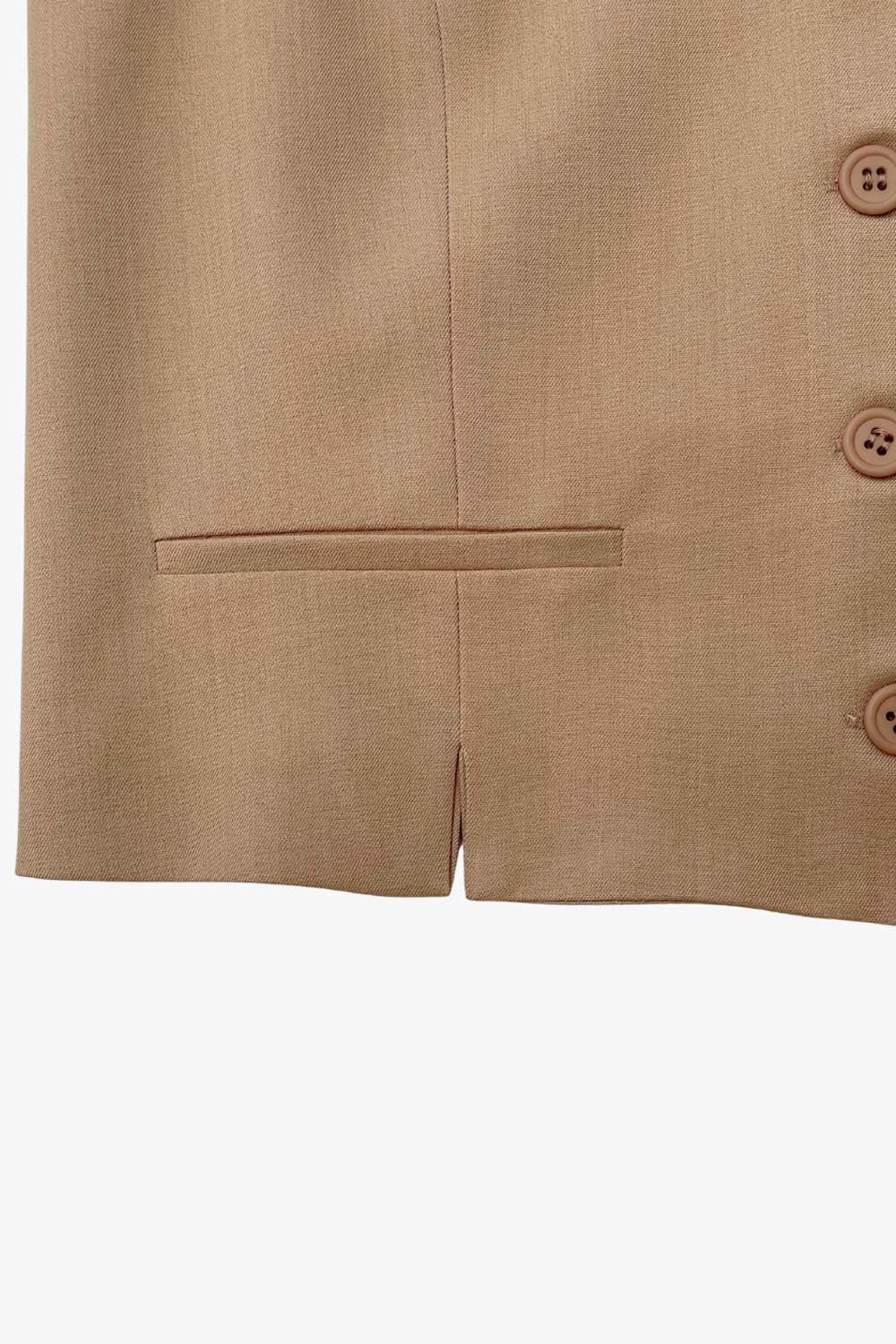 Chaleco corto de fit recto, escote v, vivos decorativos, pinzas frontales y aberturas en bajo. Detalle de trabilla ajustable posterior con hebilla y cierre frontal con hilera de botones en contraste.