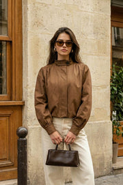 Chamarra corta de fit abullonado, cuello alto, manga larga abullonada con puño abotonado y cierre frontal con cremallera oculta. Detalle de plisados decorativos frontales y trabillas con botón en cuello.