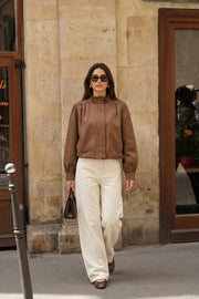 Chamarra corta de fit abullonado, cuello alto, manga larga abullonada con puño abotonado y cierre frontal con cremallera oculta. Detalle de plisados decorativos frontales y trabillas con botón en cuello.