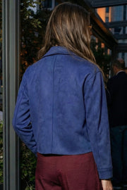 Chamarra corta de gamuza, fit recto, manga larga con puño abotonado, cuello camisero con detalle curveado, bolsillos delanteros con cartera y cierre frontal con hilera de botones en contraste.