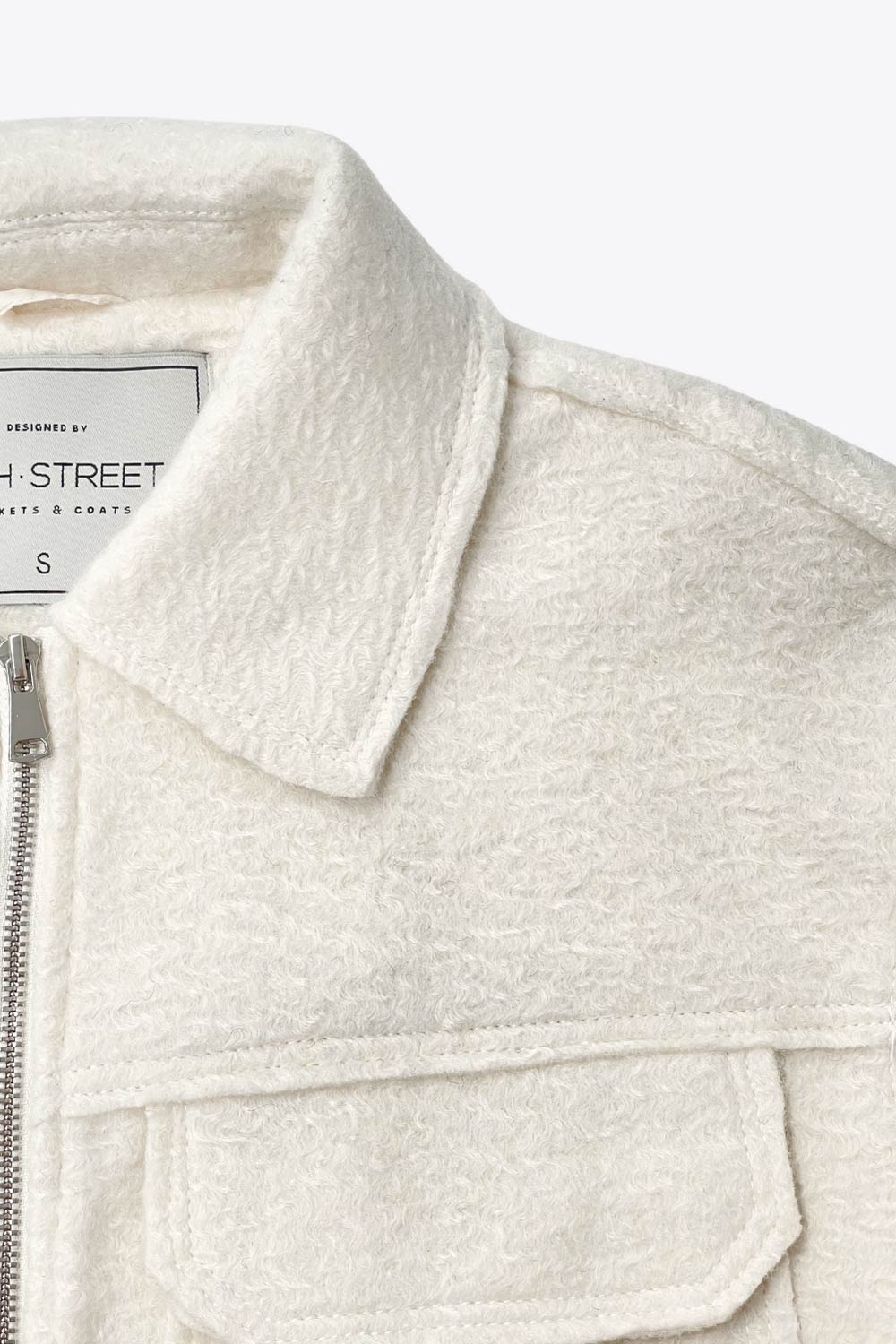 Chamarra corta de borreguillo, fit recto, manga larga con puño abotonado, cuello solapa, bolsillos frontales de parche con cartera y cierre frontal con cremallera visible en contraste.