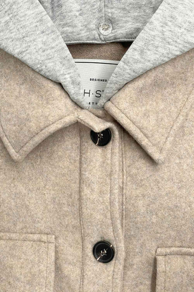 Chamarra corta de fit recto, manga larga con puño abotonado, cuello camisero, capucha en contraste, bolsillos delanteros de parche con cartera y cierre frontal con hilera de botones en contraste.