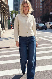 Chamarra corta de gamuza, fit oversized, cuello camisero, manga larga con puño abotonado, corte de bata frontal y posterior, bolsillos frontales de parche y cierre frontal con hilera de botones en contraste.