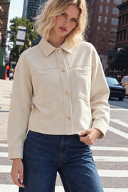 Chamarra corta de gamuza, fit oversized, cuello camisero, manga larga con puño abotonado, corte de bata frontal y posterior, bolsillos frontales de parche y cierre frontal con hilera de botones en contraste.